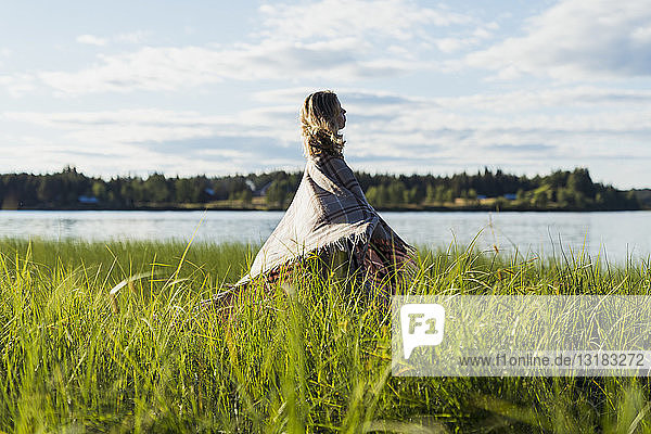 Finland  Lapland  woman wrapped in a blanket standing at the lakeside