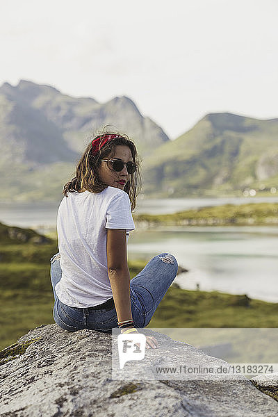 Junge Frau sitzt auf einem Felsen und schaut auf die Aussicht. Lappland  Norwegen
