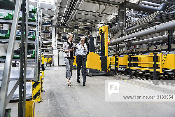 Two women with tablet walking and talking in factory shop floor