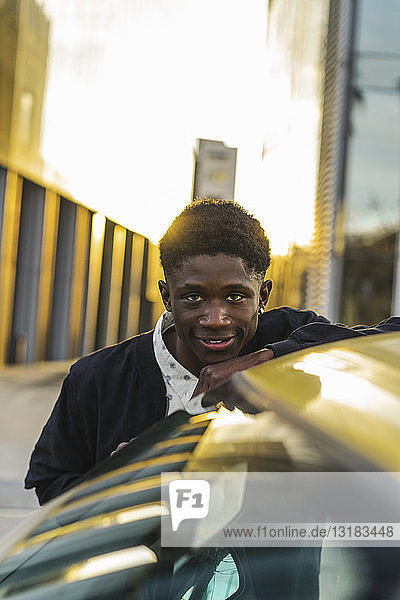 Porträt eines schwarzen jungen Mannes  der an einem Auto steht