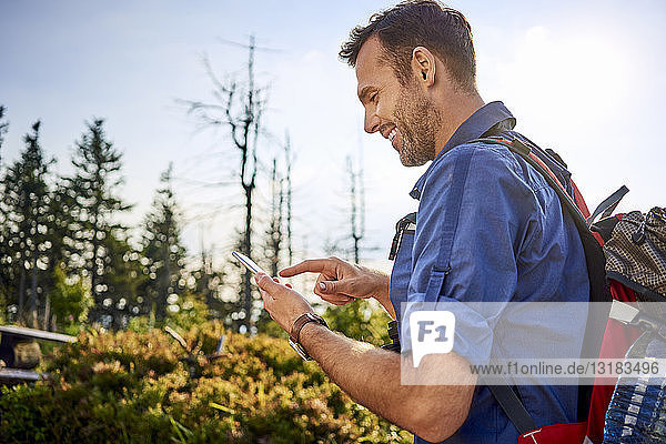 Smiling man checking his cell phone during hiking trip