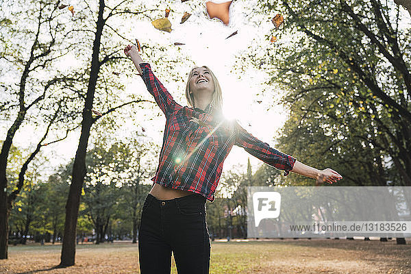 Glückliche junge Frau wirft Herbstblätter in die Luft
