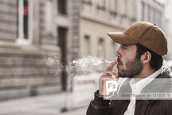 Porträt eines jungen Mannes mit Baseballmütze beim Rauchen einer Zigarette