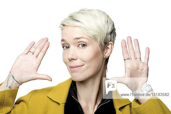 Porträt einer lächelnden Frau mit kurzen blond gefärbten Haaren vor weißem Hintergrund mit Gesten