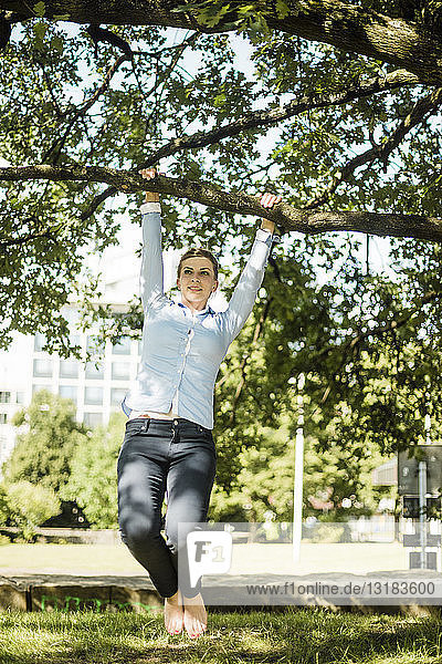 Frau im Stadtpark am Ast eines Baumes hängend