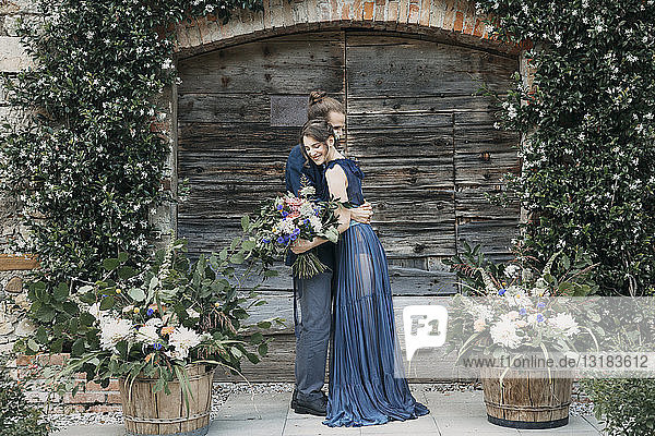 Braut und Bräutigam stehen an einem Holztor und umarmen