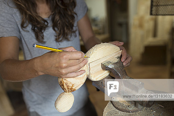 Handwerkerin  die in ihrer Werkstatt mit Bleistift auf einem Stück Holz arbeitet