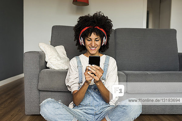 Lächelnde Frau sitzt zu Hause mit Kopfhörern und Handy