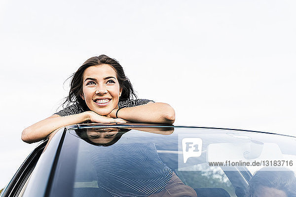 Lächelnde junge Frau schaut aus dem Schiebedach eines Autos