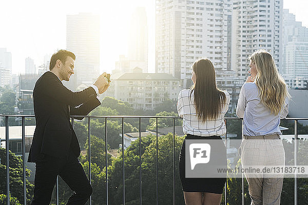 Businessman taking picture of his female colleagues on city rooftop