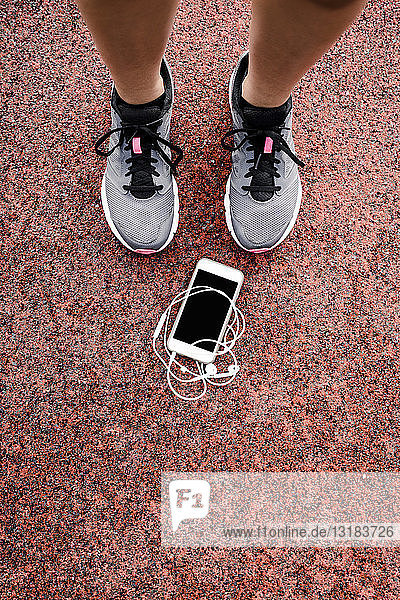 Lags of a teenage runner with smartphone and earphones lying on ground