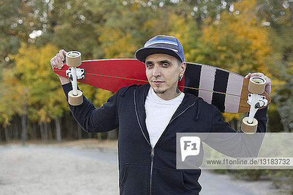 Portrait of man with skateboard on shoulders in autumn