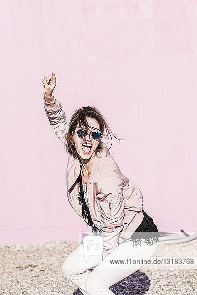 Glückliche junge Frau gestikuliert vor rosa Wand