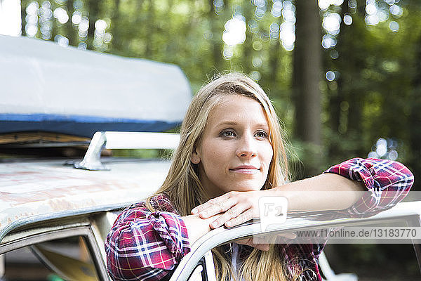 Lächelnde junge Frau beim Auto im Wald