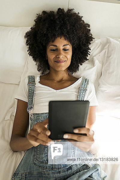 Lächelnde Frau liegt im Bett und liest E-Book
