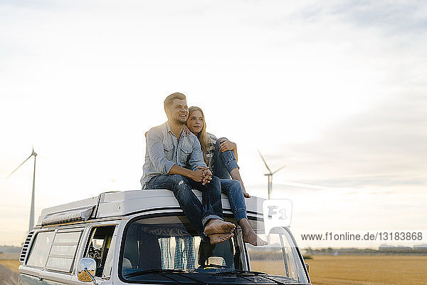 Lächelndes junges Paar auf dem Dach eines Wohnmobils in ländlicher Landschaft