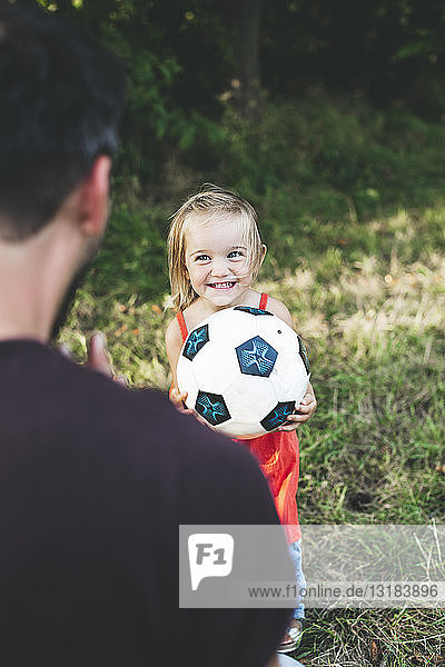 Glückliches Mädchen spielt mit Vater auf der Wiese Fussball