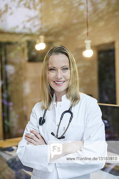 Portrait of smiling female doctor with stethoscope behind windowpane