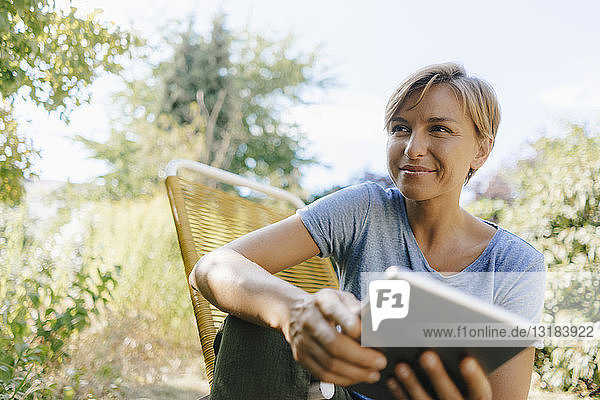 Woman sitting in garden on chair holding tablet