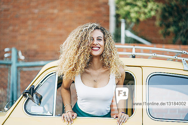 Portrait of happy blond woman leaning out of window of classic car