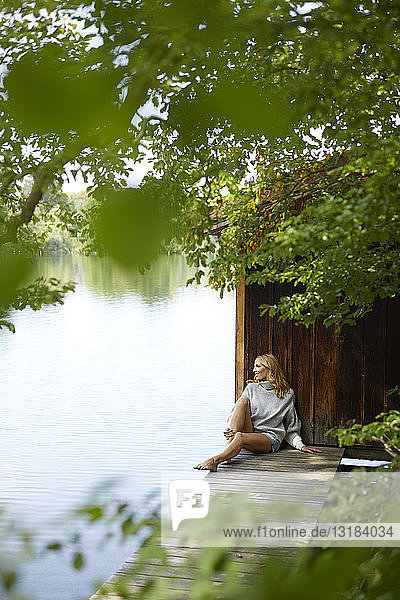 Entspannte Frau sitzt auf einem Holzsteg an einem abgelegenen See
