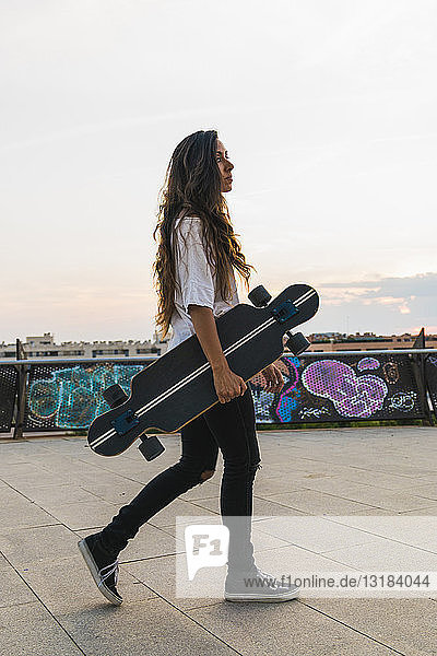 Junge Frau geht mit Skateboard in der Stadt