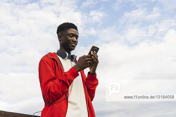 Junger Mann mit Kopfhörern  der Textnachrichten auf seinem Smartphone abliest