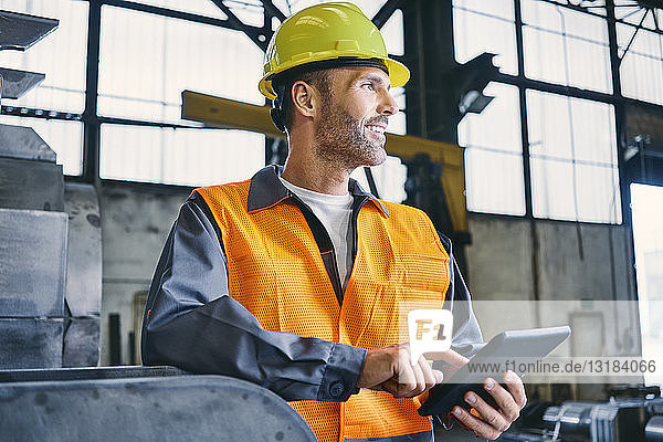 Lächelnder Mann mit Tablette trägt Arbeitsschutzkleidung in der Fabrik