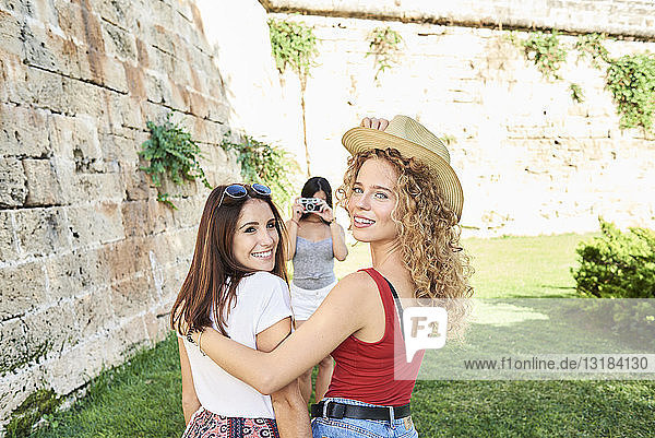 Spanien  Mallorca  Palma  zwei Freundinnen  die in die Kamera lächeln  während eine andere Freundin ein Foto von ihnen macht