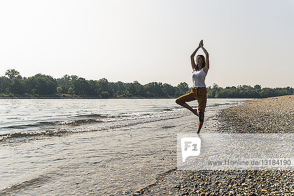 Junge Frau  die im Wasser eines Flusses steht und Yoga praktiziert
