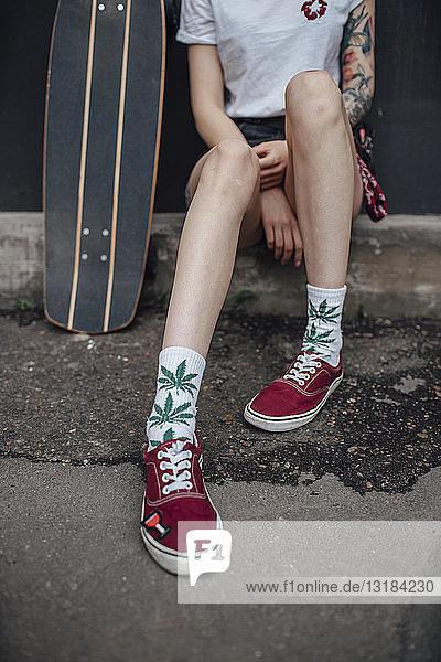 Woman's legs in socks and sneakers sitting next to carver skateboard