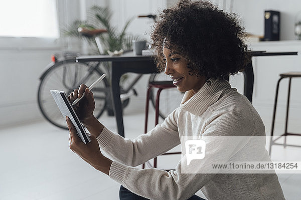 Disignerin  die auf dem Boden ihres Heimbüros sitzt und ein digitales Tablet benutzt