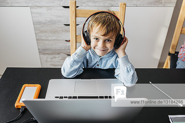 Kleiner Junge sitzt am Tisch mit Kopfhörern und Laptop