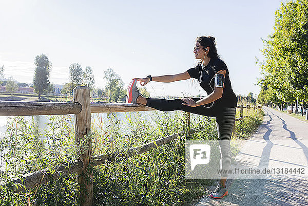 Sportliche junge Frau streckt ihr Bein am Flussufer
