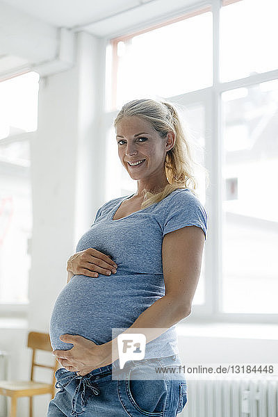 Porträt einer lächelnden schwangeren Frau am Fenster stehend