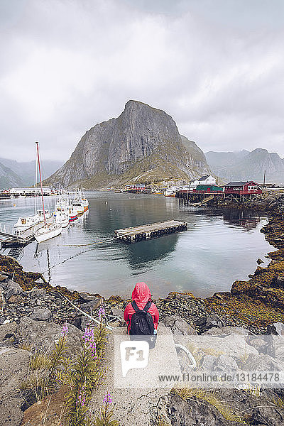 Norwegen  Lofoten  Hamnoy  Rückenansicht eines Mannes mit roter Regenjacke und Rucksack im Blick