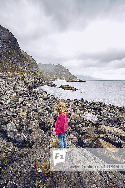 Norwegen  Lofoten  junge Frau in Regenjacke auf einem Felsen stehend