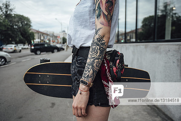 Nahaufnahme einer jungen Frau  die ein Carver-Skateboard auf dem Bürgersteig hält