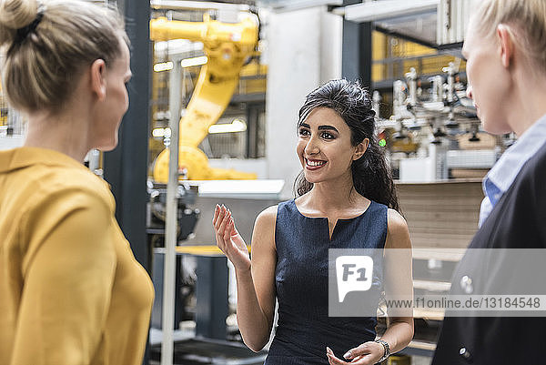 Porträt einer lächelnden Frau im Gespräch mit Kollegen in einer modernen Fabrik