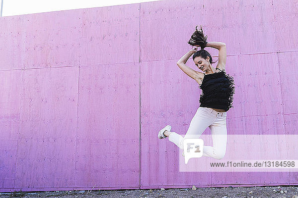 Überschwängliche junge Frau springt vor rosa Wand
