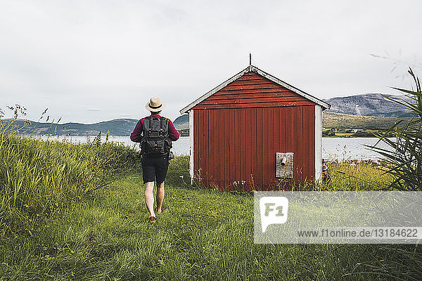 Junger Mann mit Rucksack erkundet rote Scheune in Nordnorwegen