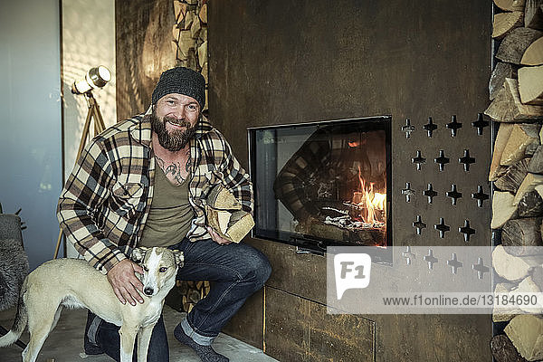 Porträt eines lächelnden Mannes mit seinem Hund vor dem Kamin zu Hause