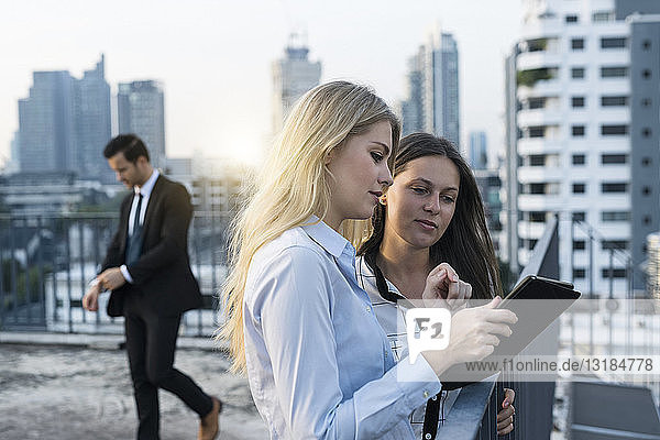 Zwei Geschäftsfrauen im Gespräch auf dem Dach der Stadt  mit einem digitalen Tablet