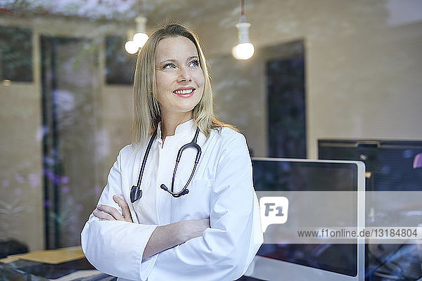 Lächelnde Ärztin mit Stethoskop hinter Fensterscheibe