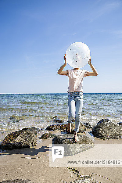 Mädchen steht auf Steinen am Strand und hält einen Ballon