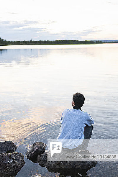 Finnland  Lappland  Mann sitzt auf einem Felsen in einem See