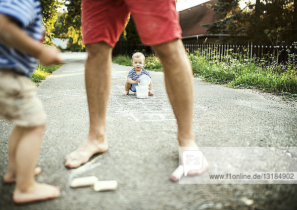 Kleines Mädchen spielt mit Eimer  während Vater und Bruder im Vordergrund stehen