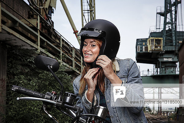 Lächelnde junge Frau setzt Motorradhelm auf