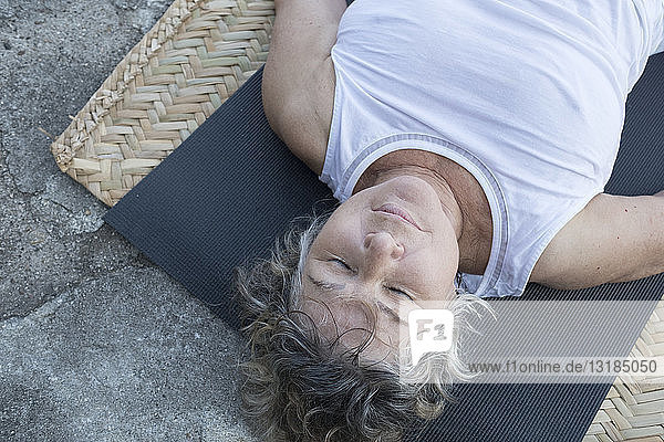 Ältere Frau liegt mit geschlossenen Augen auf Yogamatte