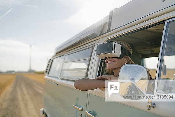 Smiling woman wearing VR glasses leaning out of window of a camper van